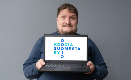 Henkilö pitää vartalonsa edessä kannettavaa tietokonetta, jonka näytöllä on Koodia Suomesta -logo.